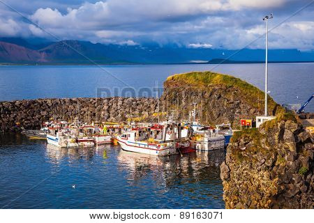 Sunset on the sea fjord in Iceland. White fishing boat in the harbor pier village Arnastapi