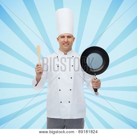 cooking, profession and people concept - happy male chef cook holding frying pan and spatula over blue burst rays background