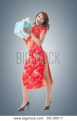 Smiling Chinese woman dress traditional cheongsam standing and holding a gift box at New Year, full length portrait isolated.