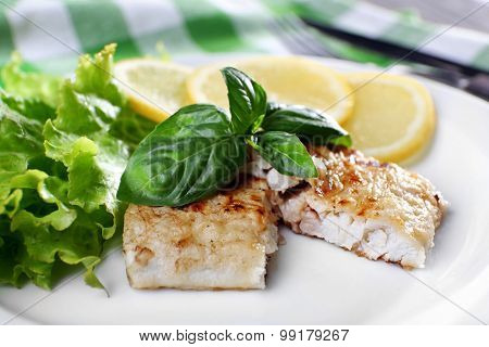 Dish of fish fillet with greens and lemon on plate close up