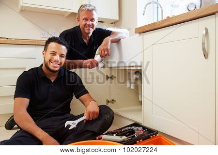 Portrait of plumber with apprentice in domestic kitchen