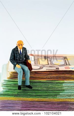 symbolic photo for retirement and old-age security, figure an old man sitting on a stack of bills