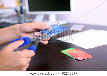 Woman's hands cutting bank card with scissors on wooden table background
