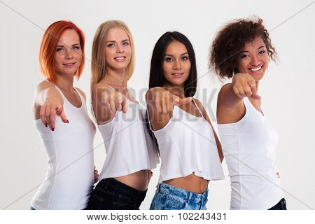 Portrait of a four multi etchnic women pointing fingers at camera isolated on a white background