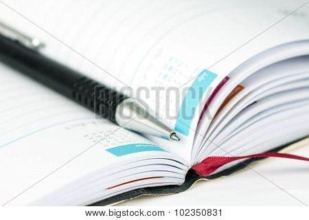 Selective Focus Of Ball Pen On Opened Lined Diary Book With Calendar Page