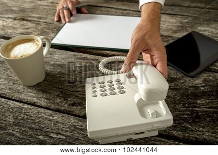 Business Person With Blank Paper And Cup Of Fresh Coffee Infront Of Him About To Make A Phone Call