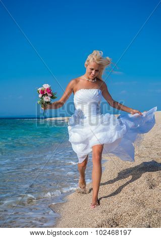 Young bride in wedding drees having fun on the beach in Greece