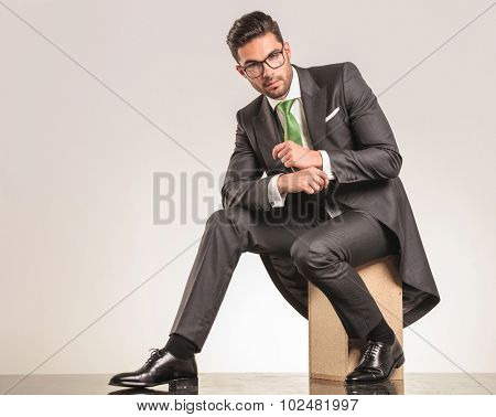 Side view of a elegant business man sitting on a wood box while fixing his sleeve.