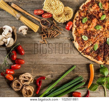 Italian food background with pizza, raw pasta and vegetables on wooden table