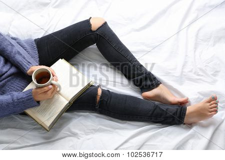 Woman on the bed with old book and cup of coffee, top view point