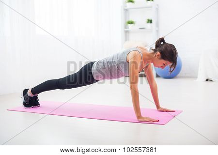fit woman doing push-ups on the floor in her living room an exercise mat at home