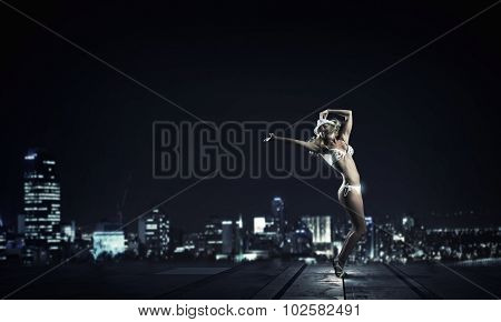 Hot young dancing woman in white bikini on night city background