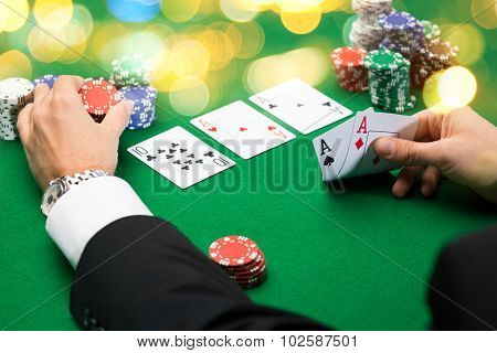 casino, gambling, poker, people and entertainment concept - close up of poker player with playing cards and chips at green casino table over holidays lights background