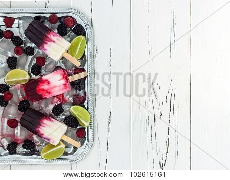 Berry vanilla ice pops - popsicles - in a vintage silver ice tray over old rustic wooden background