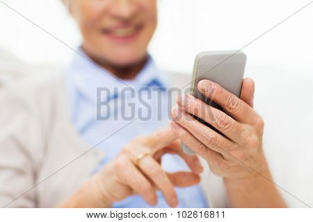 technology, communication age and people concept - close up of happy senior woman with smartphone texting message at home
