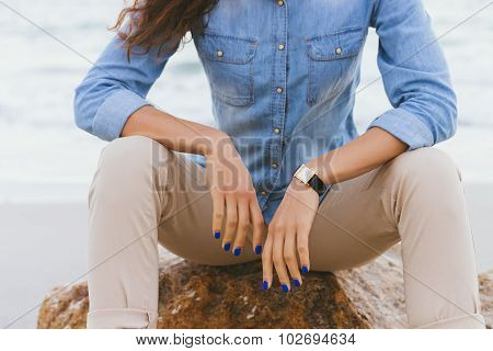 Woman In Beige Pants And A Denim Shirt Sitting On A Rock By The Sea