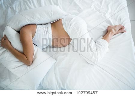 High angle view of pregnant woman with head under pillow on bed