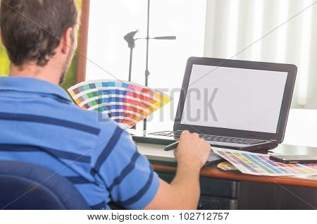 Man working on laptop while holding up palette, colormap from behind angle