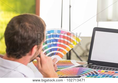 Man working on laptop while holding up palette, colormap from behind angle