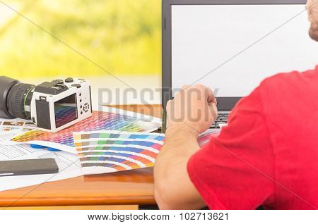 Man working on laptop with camera and palette, colormap spread out next to it