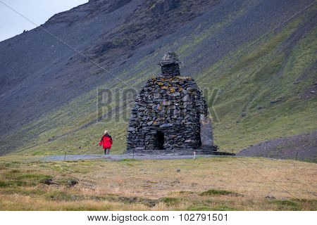 Tourist visits the rockpile structure of Bardur Snaefellsas on the clifftop at the Snaefellenes Peninsular, Iceland