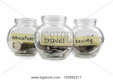 Coins In Glass Container With Travel, Saving And Education Label On White Background. Selective Focu
