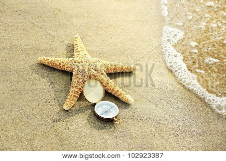 Compass with sea star on sand beach background