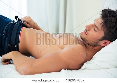 Portrait of a young man dressing jeans on the bed at home