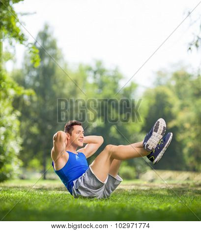 Young athlete doing sit-ups with raised legs in a park on a beautiful summer day shot with tilt and shift lens