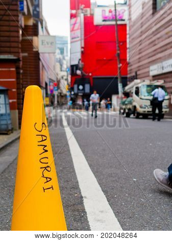 HAKONE, JAPAN - JULY 02, 2017: Close up of a word samurai written in a yellow cone in the streets with unidentified people walking behind at Hakone town, in Japan.