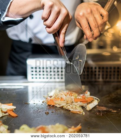 Hand Of Chef Cooking Salad On Hot Pan In Front Of Customers.