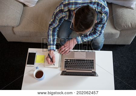 Freelancer man working working at home, making notes in notebok. Remote work at home, male doing job at home.