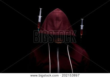 An addict male with syringes full of red liquid drugs near him on a saturated black background. A hopeless drug addict is going through addiction crisis. Depression, abuse, fear concept.