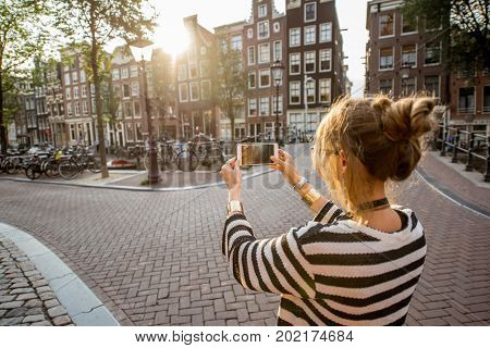 Woman tourist photographing with phone morning cityscape in Amsterdam