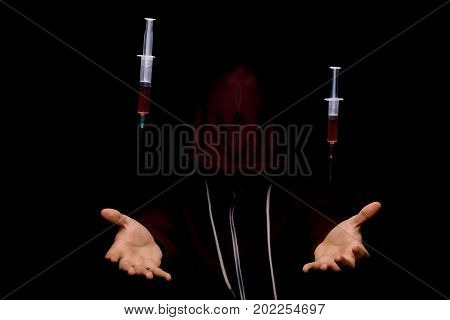 A narcomaniac guy in a dark red hoodie hallucinating in a drug overdose. Young man with drug syringes on a black background. Cocaine, meth, cannabis, LSD, ecstasy, morphine addiction concept.