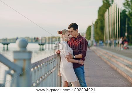 A beautiful blonde in a pink dress with her handsome guy in a red shirt is good at spending time near river