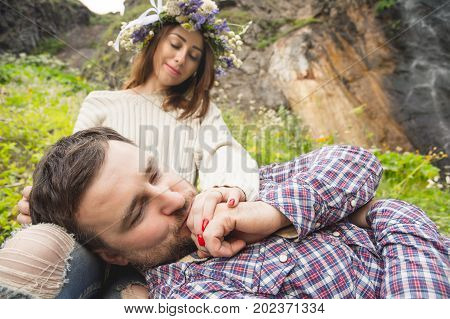 Hipster with a beard lies on the lap of his girl who wears a vinok of wildflowers. The concept of unity with nature and a young couple of people
