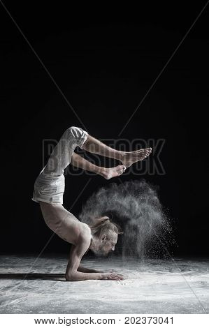 Flexible yoga man doing hand balance asana vrischikasana. Dust flying in air.
