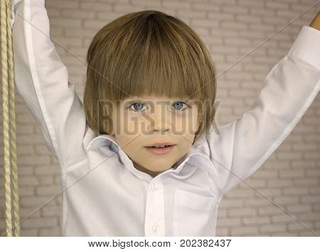Lovely cheerful boy in a white shirt close up on a light brick wall background
