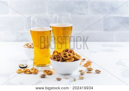Beer in glass, mini pretzel and pistachio on white stone background. Copy space