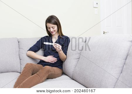 A girl sitting on a couch at home while reading the results of her recent pregnancy test