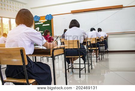Asian School students in uniform taking examination and writing answer sheet in classroom educational school view of having exams in class on seat rows Education system tests concept of Thailand