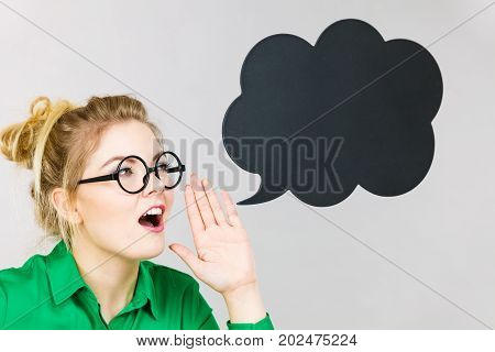 Business woman wearing green shirt and eyeglasses yelling telling something someone black thinking or speech bubble next to her.
