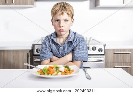 lovely boy showing boring expression with fresh colorful vegetables