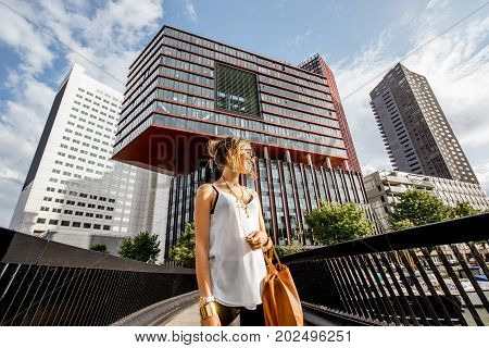 Lifestyle portrait of a young woman walking the bridge at the modern district with slyscrapers in Rotterdam city