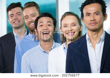 Excited funny Asian male manager with open mouth standing among colleagues and looking at camera. Joyful young man laughing while standing in line. Employees concept