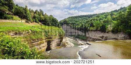 Standing at the summit of the middle falls in Letchworth State Park in Castile NY along the Genesee river looking down the valley of the gorge. This photo was taken in the summer time when everthing is green and the flowers are blooming.