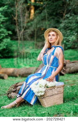 Beautiful girl wearing blue dress collect flowers in basket in the green grass wood
