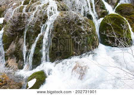 Waterfall in the forest. Frozen water drains over the rocks. The rock is covered with moss on which cold water flows.Rock in moss. The rock in the moss on which the water flows down