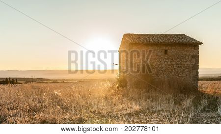 Romantic sunset above and french farmland with stubble of sunflowers and an old farmhouse in the middle of the landscape.
